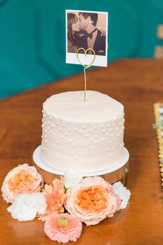 a white wedding cake with flowers and a photo on top is sitting on a table