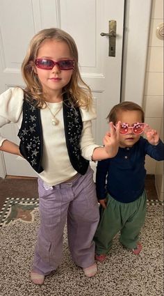 two young children standing next to each other in front of a door with sunglasses on