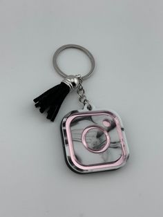 a pink and black square shaped keychain with a tassel