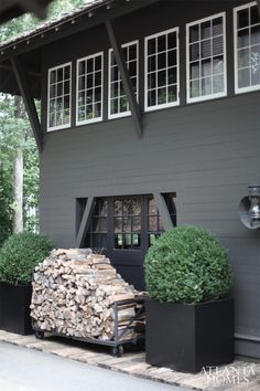 two large black planters filled with logs in front of a gray house on a sunny day