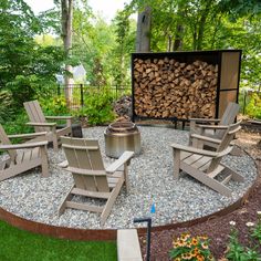 an outdoor fire pit surrounded by lawn chairs and stacked logs in the back yard area