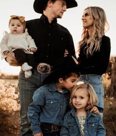 a man and woman with two children in their arms posing for a family photo while wearing cowboy hats