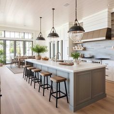 a large kitchen with an island and bar stools in it, along with several lights hanging from the ceiling