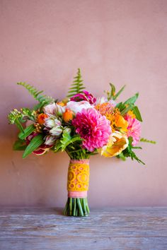 a bouquet of colorful flowers sitting on top of a wooden table next to a wall