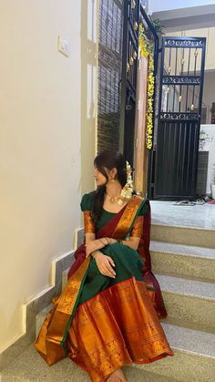 a woman sitting on the steps wearing a green and orange sari with gold accents