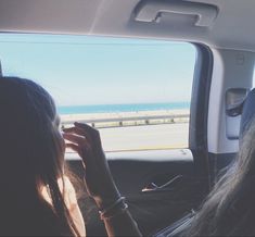 two women are sitting in the back seat of a car looking out at the ocean