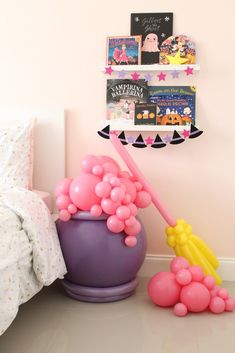 a pink and purple balloon filled bucket next to a book shelf with books on it