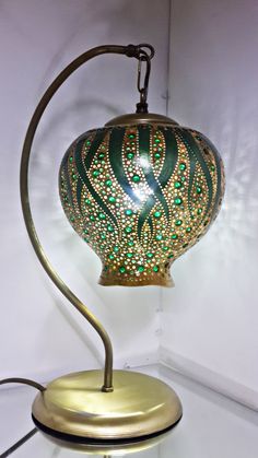 a green and gold table lamp on a white wall next to a light fixture that is shaped like an ornament