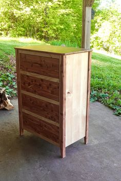 a tall wooden dresser sitting on top of a cement floor next to a green field