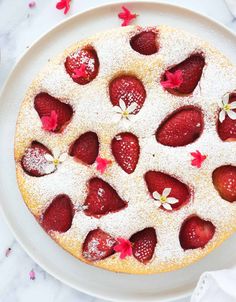 a white plate topped with a cake covered in powdered sugar and sliced strawberries