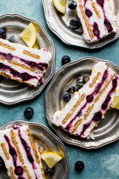 four slices of cake with blueberries and lemons on them sitting on silver plates