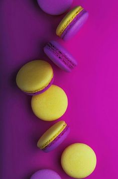 three macaroons are lined up on a purple surface with pink and yellow frosting