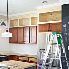 a kitchen with wooden cabinets and ladders in the foreground, chalkboard on the wall