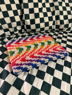 a colorful pillow sitting on top of a bed covered in checkered sheets