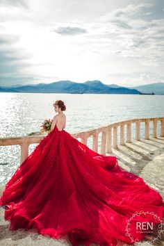 a woman in a red dress is standing on a pier by the water with her back to the camera