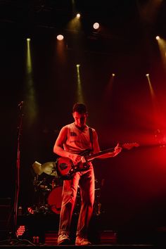 a man standing on stage with a guitar in front of red and green lights behind him