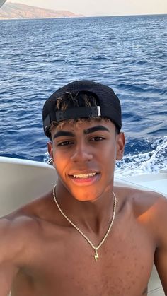 a shirtless young man sitting on a boat in the ocean wearing a black hat