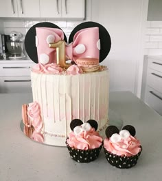 two cupcakes with pink frosting and minnie mouse ears are on top of a cake