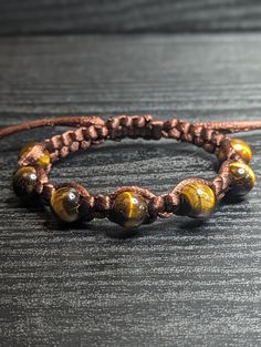 Beautiful high-quality natural yellow/brown 10mm Tigers Eye gemstone macrame bracelet. This piece is assembled with a dark brown satin nylon cord and is finished with a slide-adjustable closure. This beautiful macrame piece would make a great gift!  Tiger's Eye is known for its grounding, protective, and harmonizing properties. It is said to encourage self-confidence, promote mental clarity, and attract abundance and prosperity. Tigers Eye stone is known for its ability to shield against negativ Brown Adjustable Waxed Cord Bracelet, Adjustable Handmade Brown Braided Bracelet, Brown Bracelet With Adjustable Cord, Brown Braided Bracelets With Adjustable Waxed Cord, Brown Waxed Cord Braided Bracelets With Adjustable Cord, Brown Adjustable Braided Waxed Cord Bracelets, Brown Adjustable Cord Bracelets, Brown Braided Bracelet With Sliding Knot, Adjustable Brown Bracelets With Sliding Knot