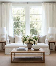 a living room filled with white furniture and flowers on top of a wooden coffee table