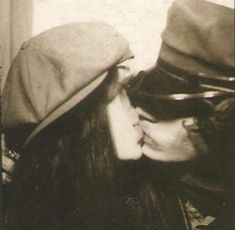 an old photo of two people kissing each other with hats on their heads and one woman's face to her left