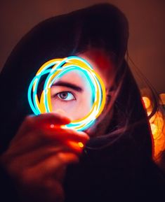 a woman looking through a magnifying glass with neon lights on her face in front of her