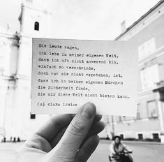 a person holding up a piece of paper with a poem on it in front of a building