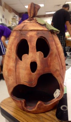 a wooden carved pumpkin with its mouth open on a table in a room full of people