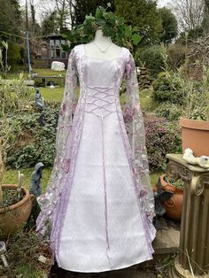 "FASHIONED FROM  A  LUXURIOUS TRULEY GORGEOUS LILAC CRUSHED VELVET  (CONTAINING LYRCA) ...     IDEAL FOR  A  MEDIEVAL / RENAISSANCE THEMED BALL, PARTIES, summer jousts, HANDFASTINGS / WEDDINGS, OR ANY SPECIAL, SACRED OCCASSION, FOR THAT EXTRA WOW FACTOR     THE FRONT PANEL HAS BEEN FASHIONED FROM A TRULY GORGEOUS STUNNING AND UNIQUE WHITE JACQUARD WITH A BEAUTIFUL PALE LILAC  EMBROIDERED DELICATE SCROLL LEAF DESIGN  THE  FULL LENGTH MEDIEVAL  CAPE SLEEVES HAVE  BEEN FASHIONED FROM A LUXURIOUS TR Purple Fantasy Dresses For Fantasy Events, Fitted Fairycore Medieval Dress Costume, Fitted Fairytale Medieval Dress For Larp, Fitted Medieval Dress For Larp In Fairytale Style, Gothic Purple Wedding Dress, Handfasting Dress, Medieval Cape, Wedding Handfasting, Lilac Fairy