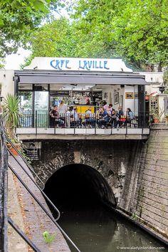 people are sitting at tables on the side of a small bridge over a canal in an urban area