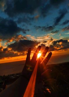 a person's hand with the sun setting in the background and clouds above them