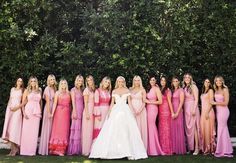 a group of women standing next to each other in front of some bushes and trees