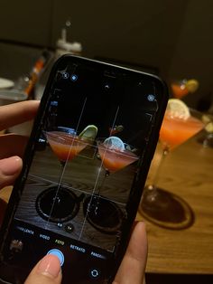 someone is holding up their cell phone to take a photo of some drinks on the table