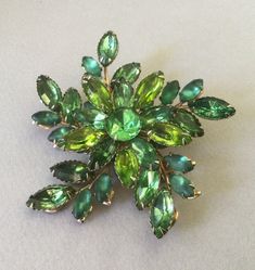 "Beautiful dimensional flower sprig pattern.  Perfect looking varying shades of green rhinestones form tendrils around a larger round center stone.  Large marquise/navette prong set clear green, blue-green, peridot green and frosted green stones seem to radiate around the edge of this good looking brooch.  It seems to catch the light in different ways. Riveted construction.   Great for evening wear.  Very elegant!  Unsigned early '50s brooch. 3\" diam 27.8 grams wt. Attention: All items are list Mid-century Green Brooch For Formal Occasions, Mid-century Green Brooches For Formal Occasions, Green Mid-century Style Brooches For Formal Occasions, Mid-century Green Formal Brooches, Antique Green Brooch For Evening, Vintage Green Brooch For Evening, Vintage Green Evening Brooch, Vintage Green Evening Brooches, Formal Green Rhinestone Brooches