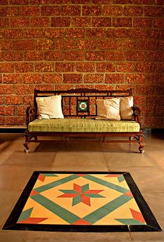 a bench sitting in front of a brick wall next to a rug on the floor