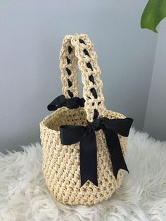 a crocheted basket with a black bow on the front and bottom, sitting on a white furnishing