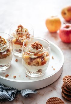 three glasses filled with dessert sitting on top of a white plate next to crackers