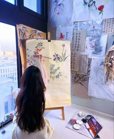 a woman is painting on an easel in front of a window