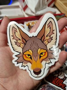 a hand holding a sticker with an image of a fox on it's face