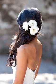 a woman in a wedding dress with flowers in her hair and back to the camera