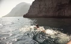 a person swimming in the ocean next to a cliff