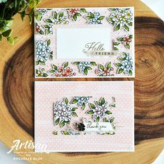 two cards with flowers on them sitting on top of a wooden table