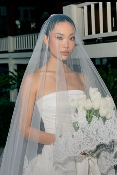 a woman in a wedding dress holding a bouquet of flowers and wearing a veil over her head