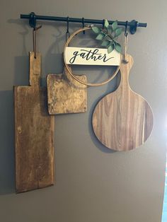 two wooden cutting boards hanging on a wall next to a sign that says gather and a potted plant