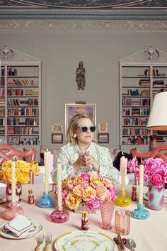 a woman wearing sunglasses sitting at a table with flowers and candles in front of her