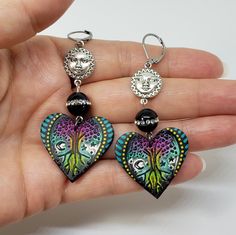 a person holding two heart shaped earrings in their hand, one with a face on it