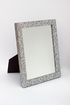 a silver glittered mirror sitting on top of a white table next to a black stand