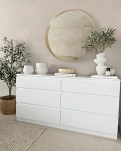 a white dresser sitting in front of a mirror and potted plant on top of it