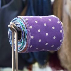 a purple and white polka dot fabric roll on a metal rack with several different colored fabrics