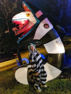 a woman is standing in front of a fake rocket ship and snake sculpture at night